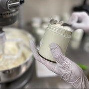 Person holding a container of cream in a kitchen setting with a mixer in the background