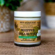 Jar of Mion Artisan Soap whipped shea butter on a wooden surface with a blurred background