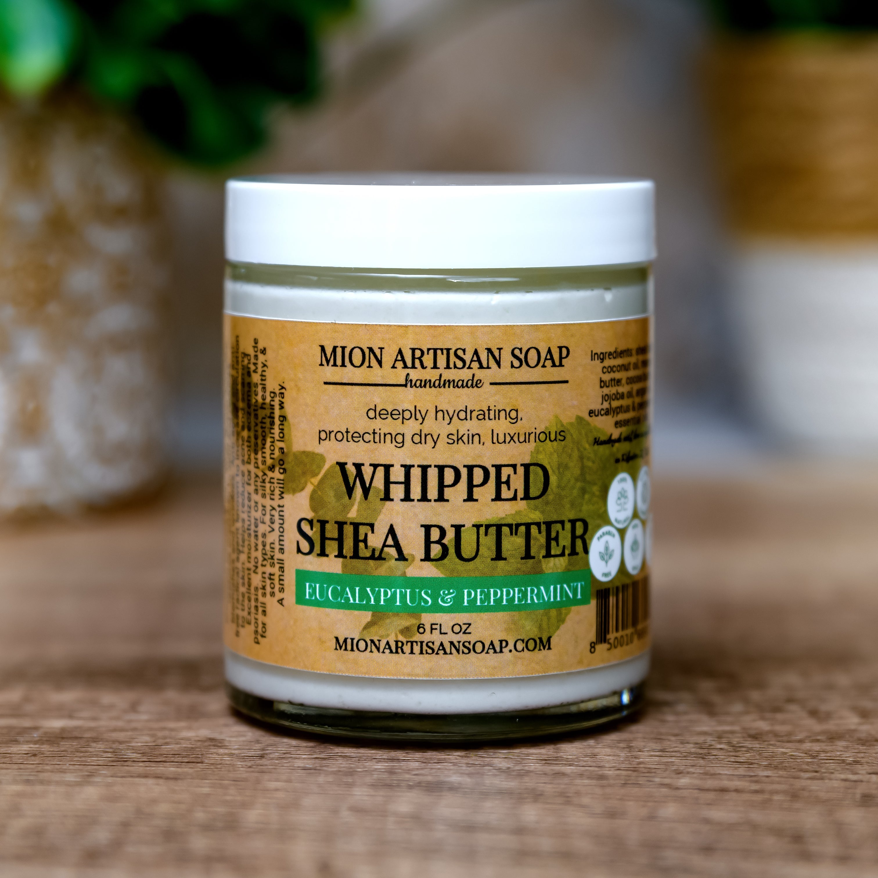 Jar of Mion Artisan Soap whipped shea butter on a wooden surface with a blurred background