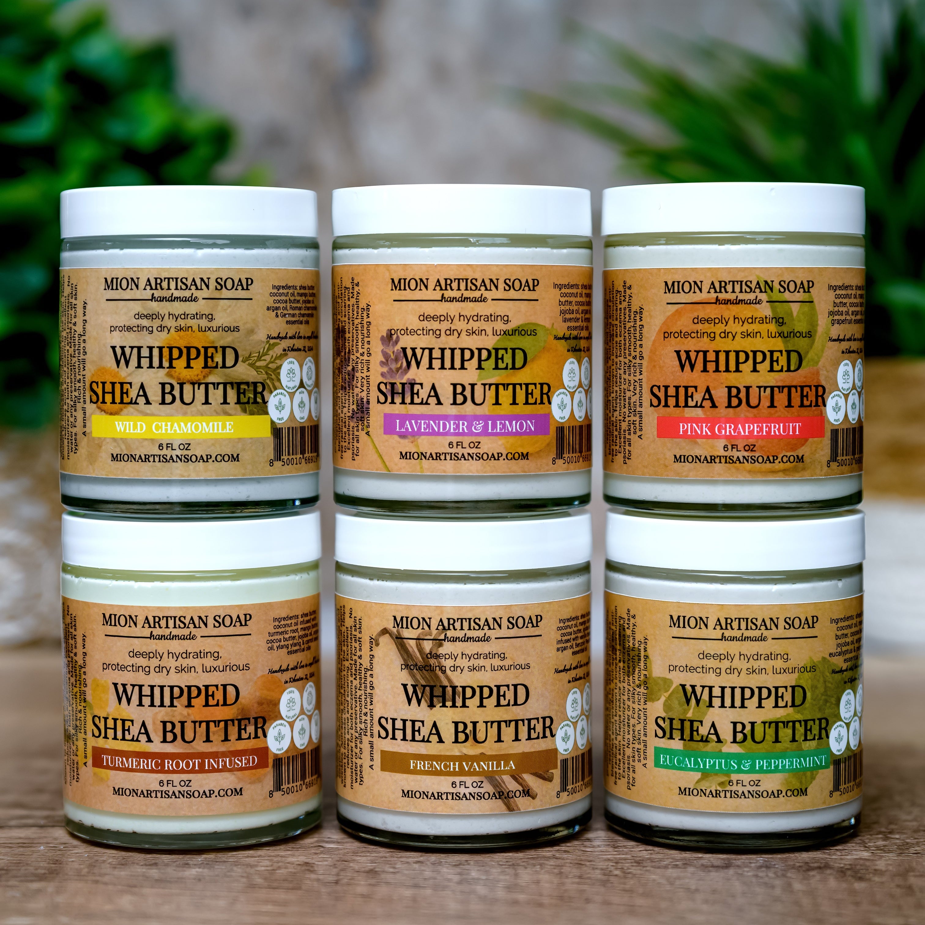 Five jars of Whipped Shea Butter from Moon Artisan Soap on a wooden surface with a blurred green plant background.
