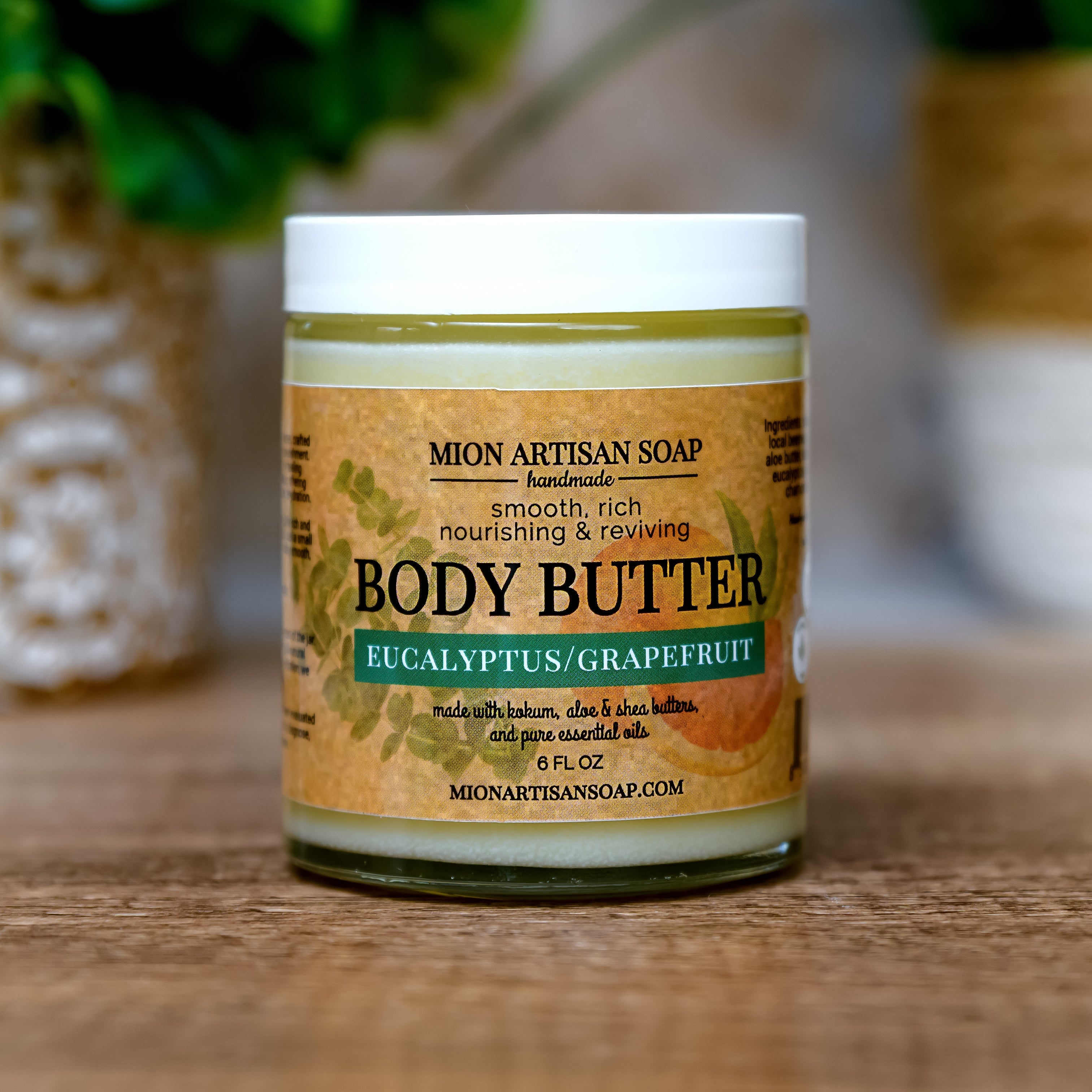 Jar of Mion Artisan Soap body butter on a wooden surface with plants in the background