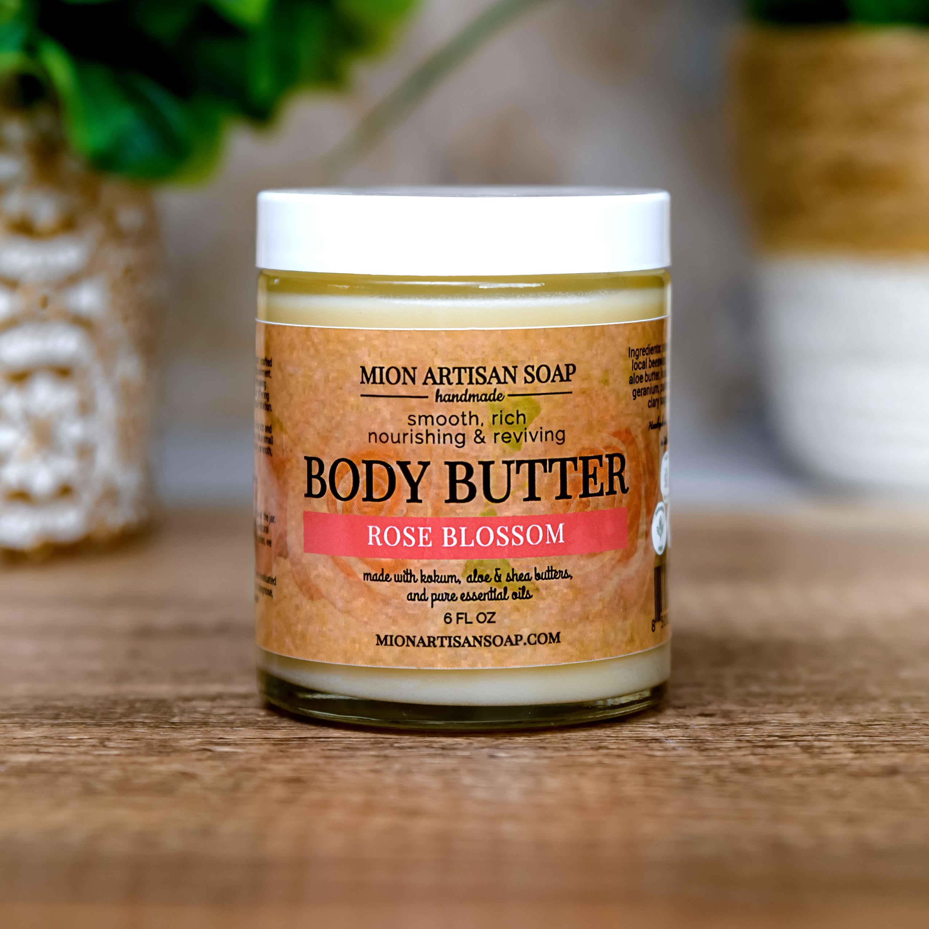 Jar of Mion Artisan Soap Body Butter with a rose blossom scent on a wooden surface.