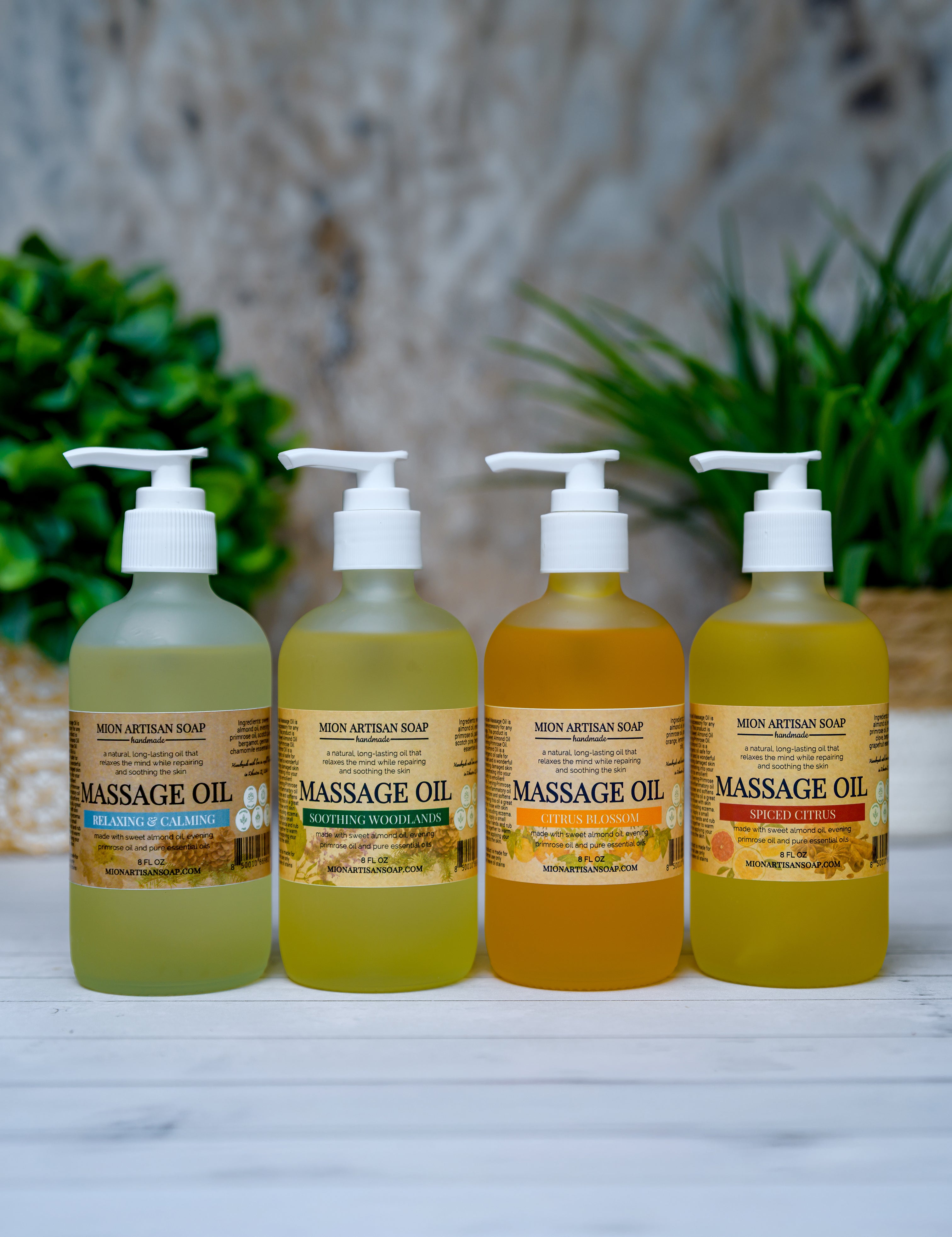 Four bottles of massage oil with different colored oils on a white surface with a blurred natural background.