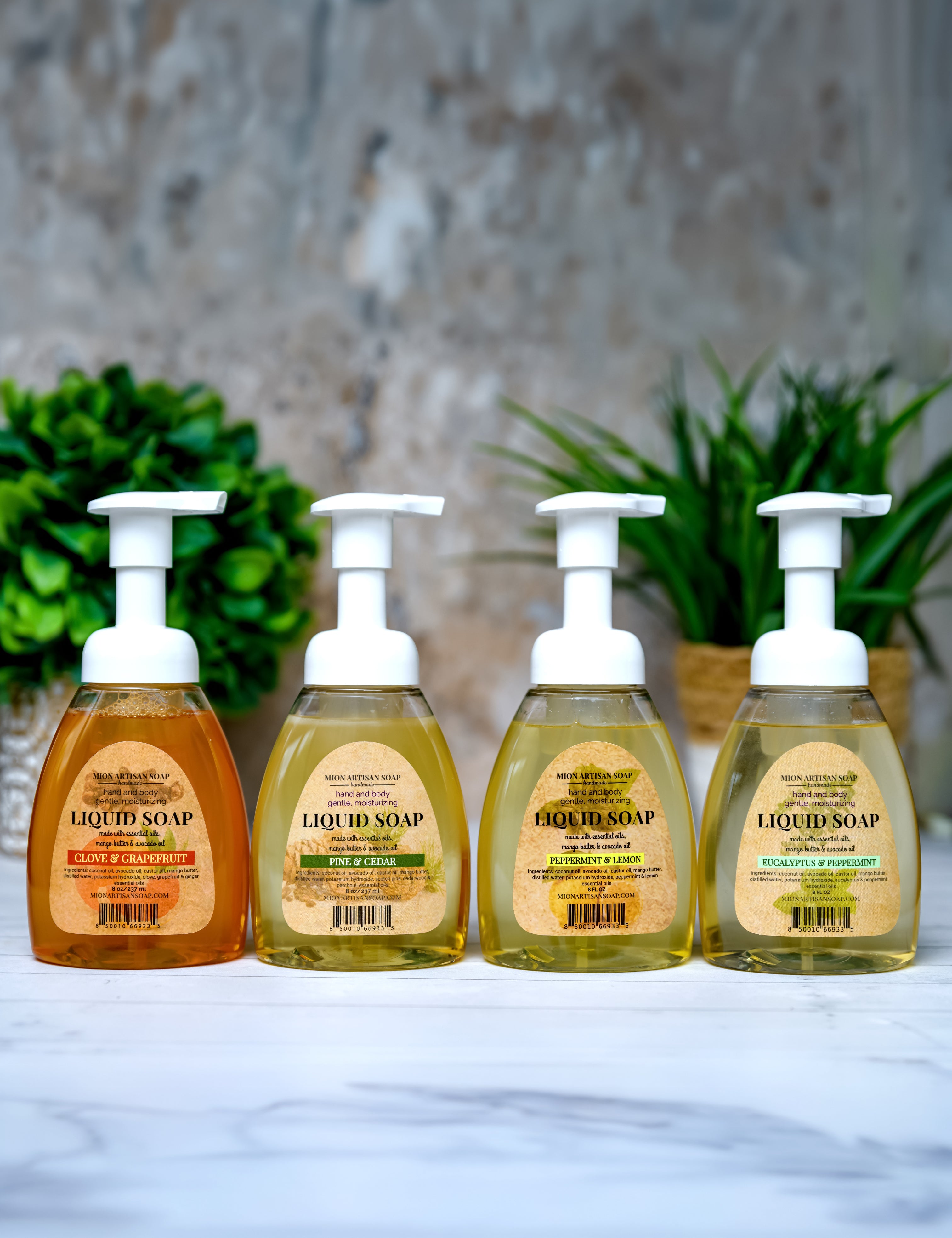 Four bottles of liquid soap with pump dispensers on a stone surface with plants in the background.