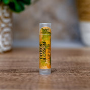 Lip balm tube labeled 'Citrus Blossom' on a wooden surface with a blurred natural background