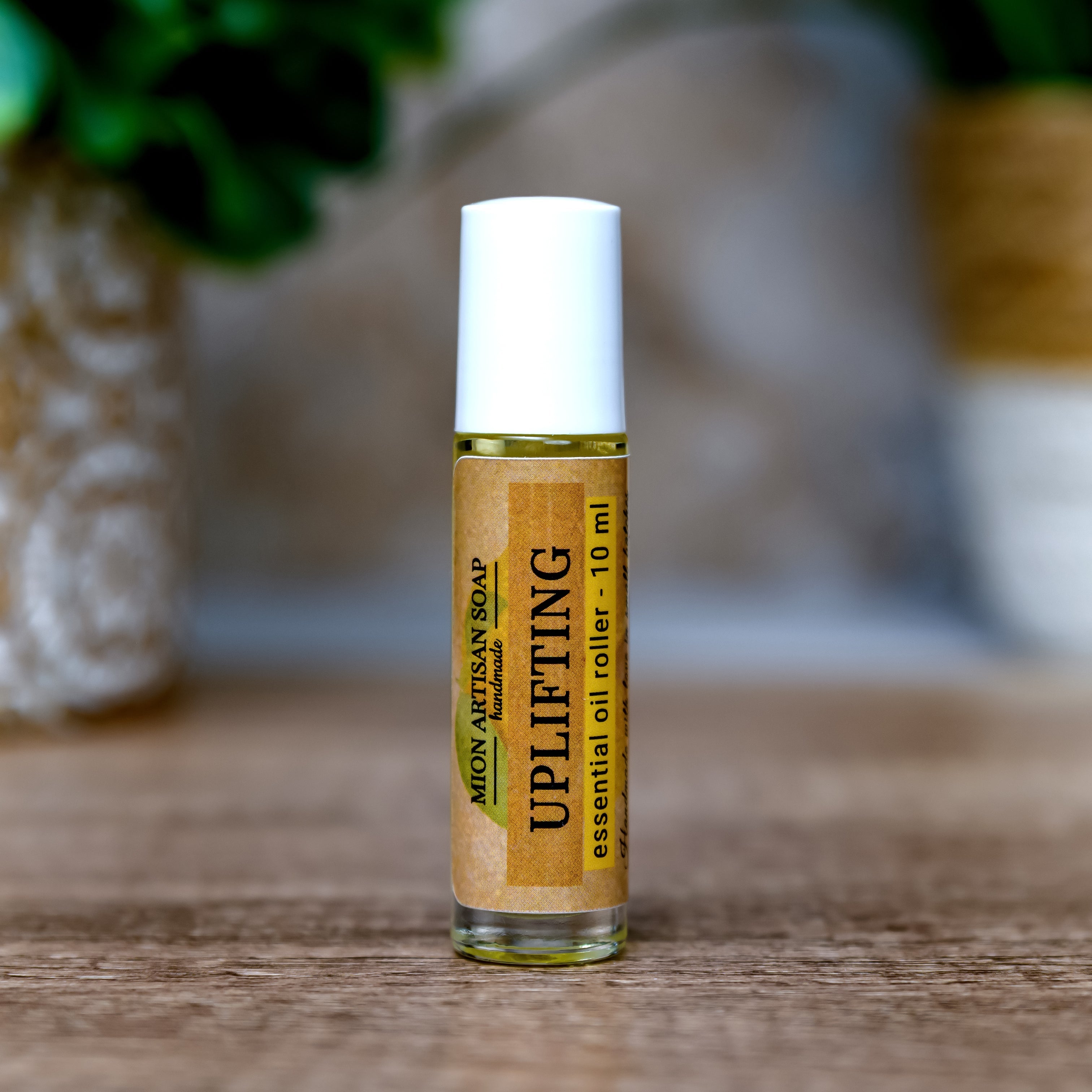 Roll-on bottle of essential oil labeled 'Uplifting' on a wooden surface with a blurred natural background.