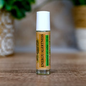 Roll-on bottle labeled 'Energy Alertness' on a wooden surface with a blurred green plant in the background.