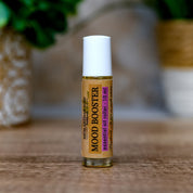 Roll-on bottle labeled 'Mood Booster' on a wooden surface with a blurred green plant in the background.