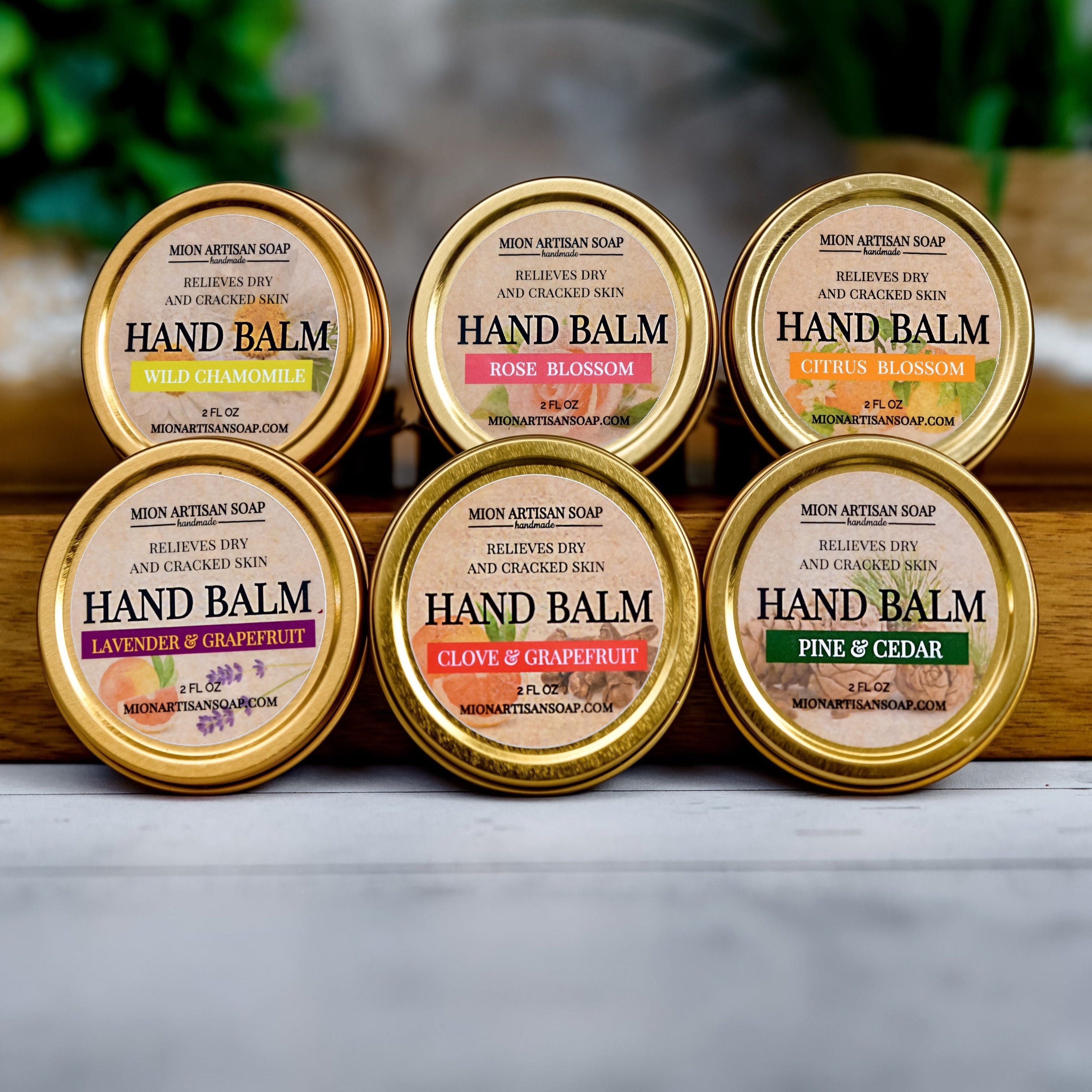 Set of six hand balm containers with various scents on a wooden surface.