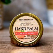 Hand balm container with 'Clove & Grapefruit' scent on a wooden surface