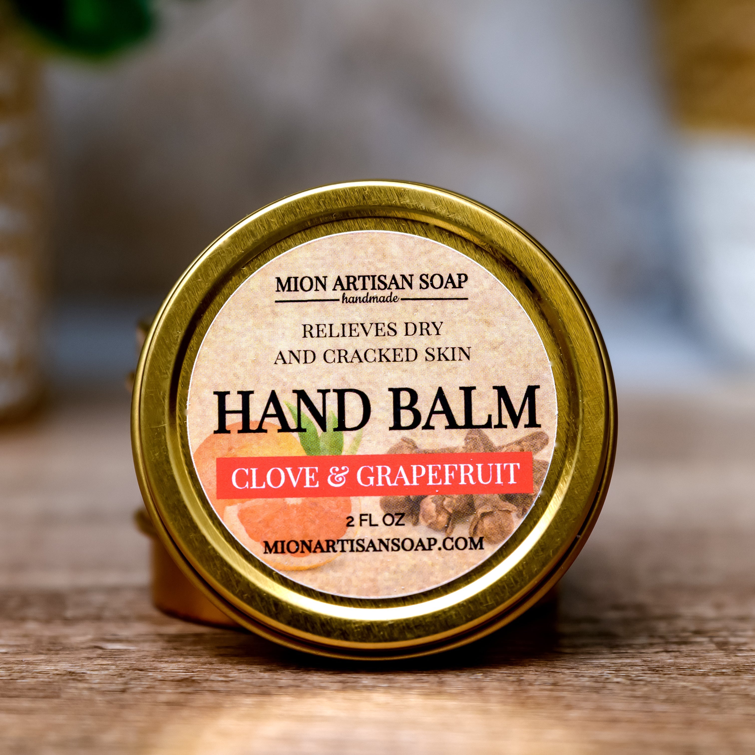 Hand balm container with 'Clove & Grapefruit' scent on a wooden surface