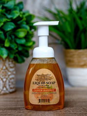 Bottle of liquid soap with a label on a wooden surface with plants in the background