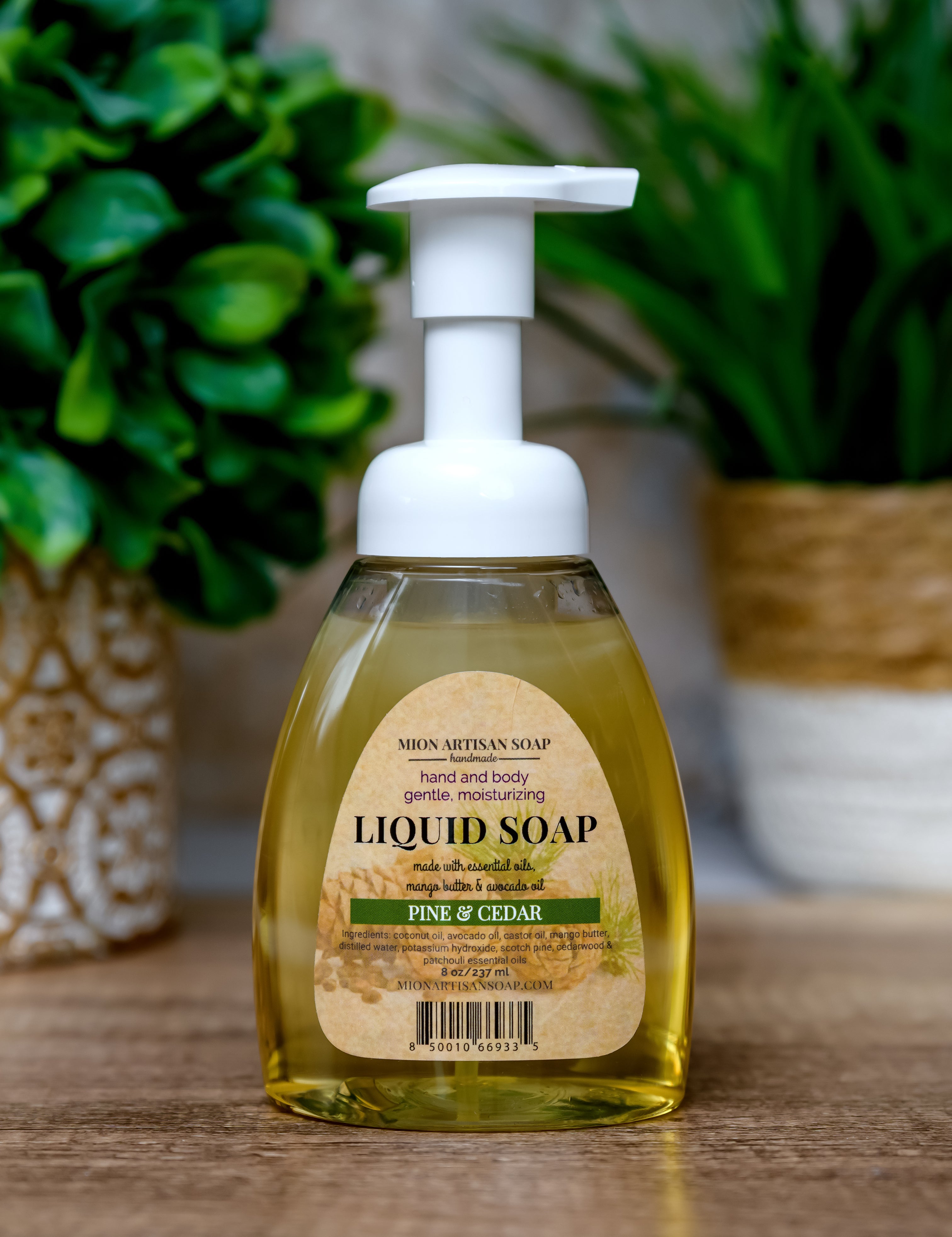 Bottle of liquid soap with a pump dispenser on a wooden surface, surrounded by green plants.