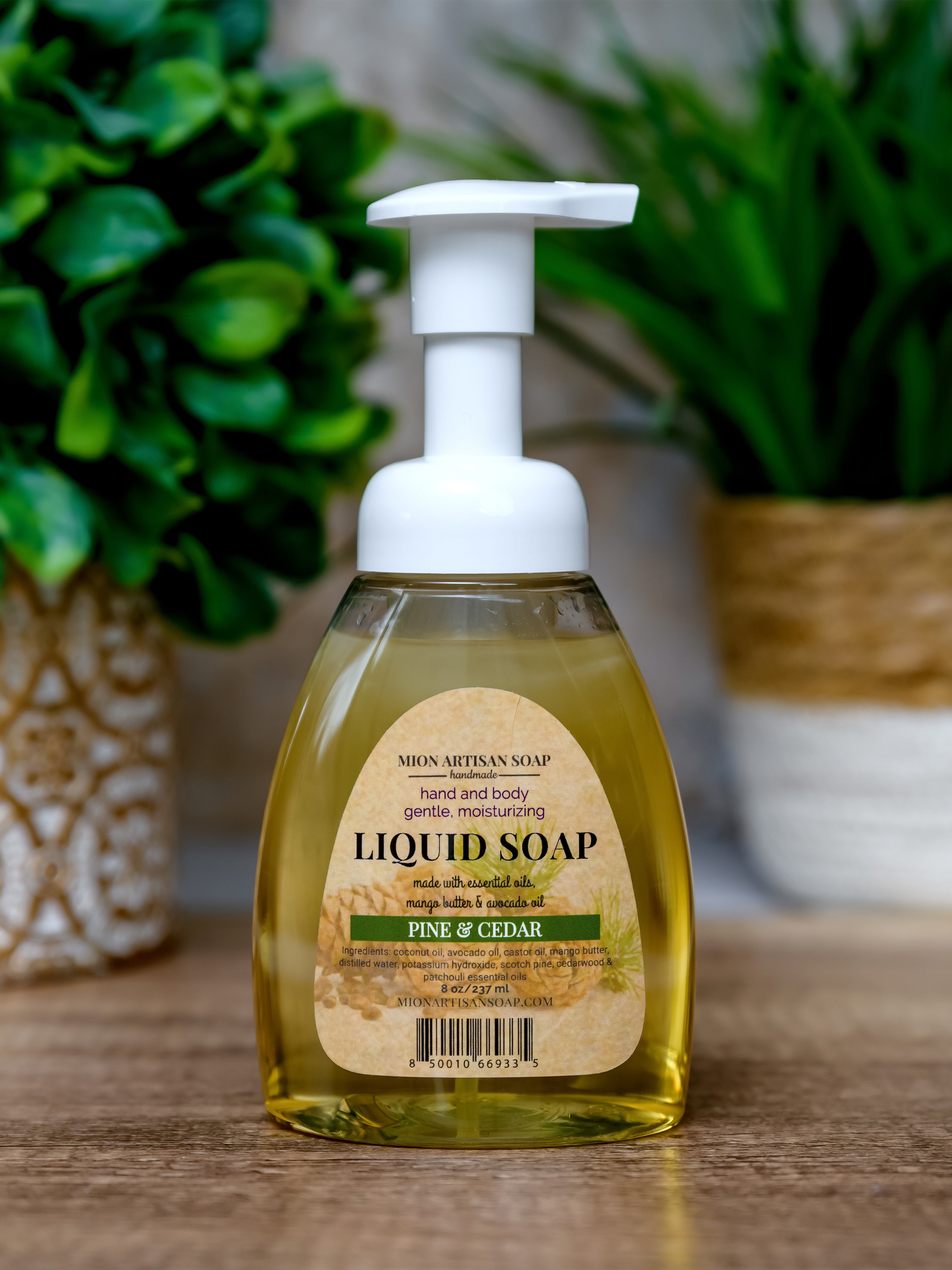 Bottle of liquid soap with a pump dispenser on a wooden surface, surrounded by green plants.