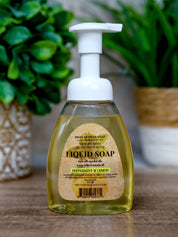 Bottle of liquid soap with a pump dispenser on a wooden surface, surrounded by green plants.