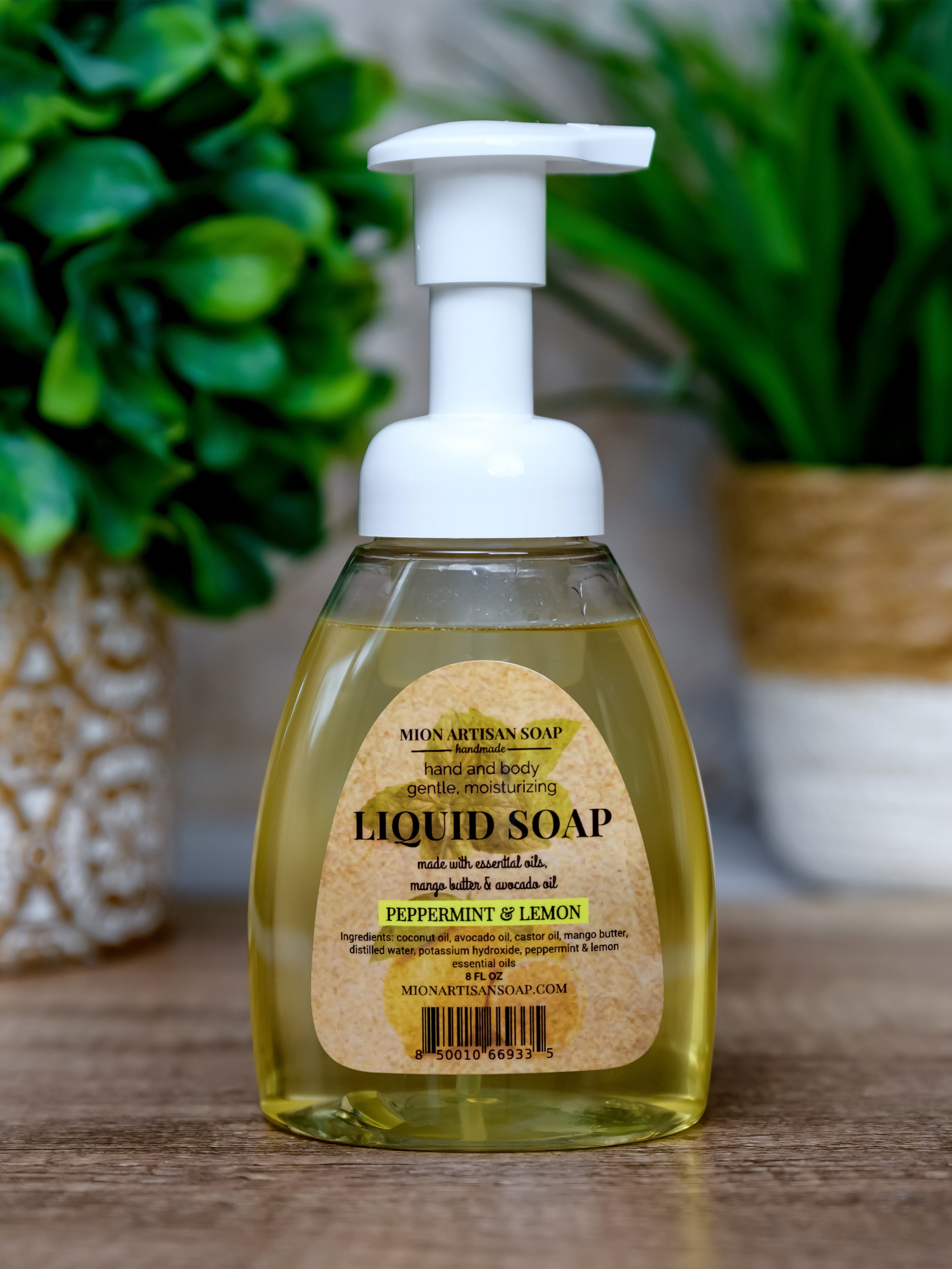 Bottle of liquid soap with a pump dispenser on a wooden surface, surrounded by green plants.