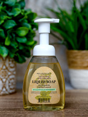 Bottle of liquid soap with a pump on a wooden surface, surrounded by green plants.