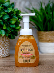 Liquid soap bottle with a white pump on a wooden surface with green plants in the background