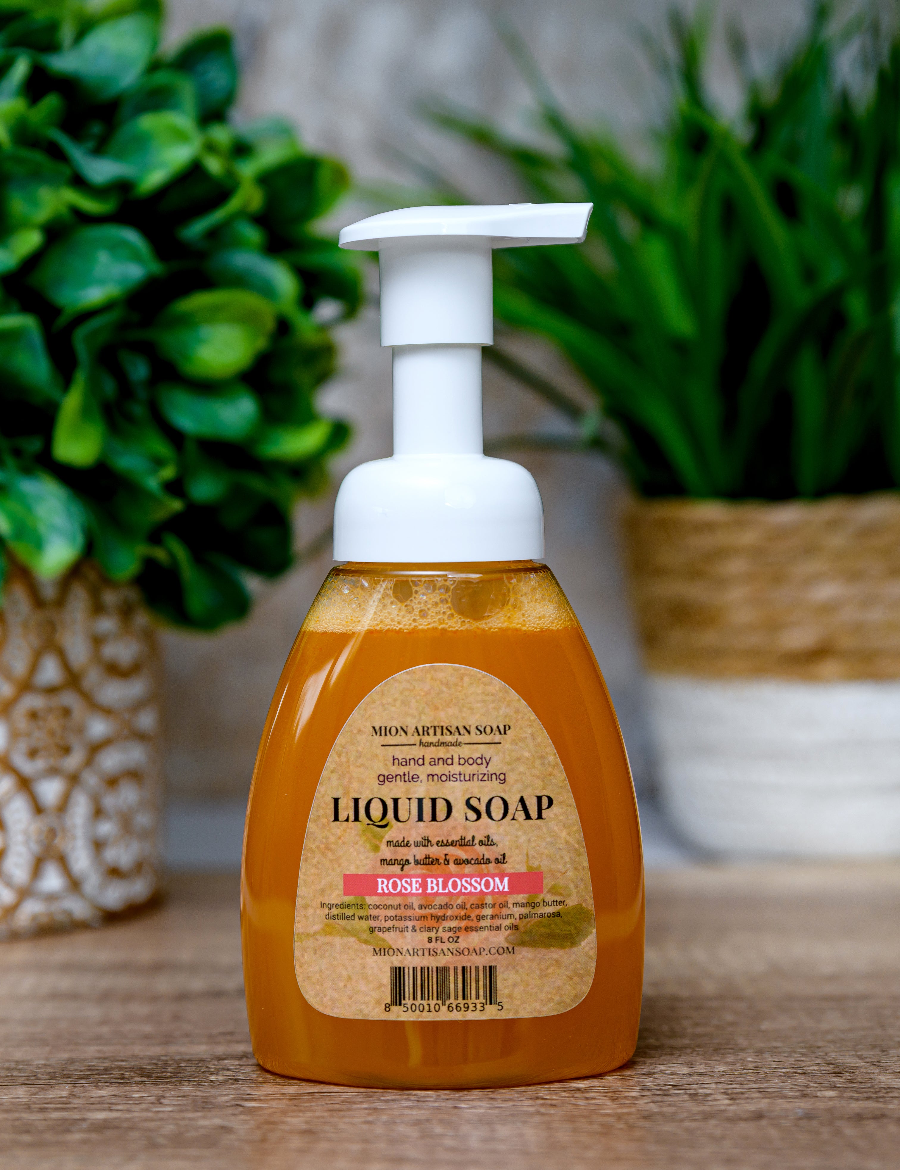 Liquid soap bottle with a white pump on a wooden surface with green plants in the background