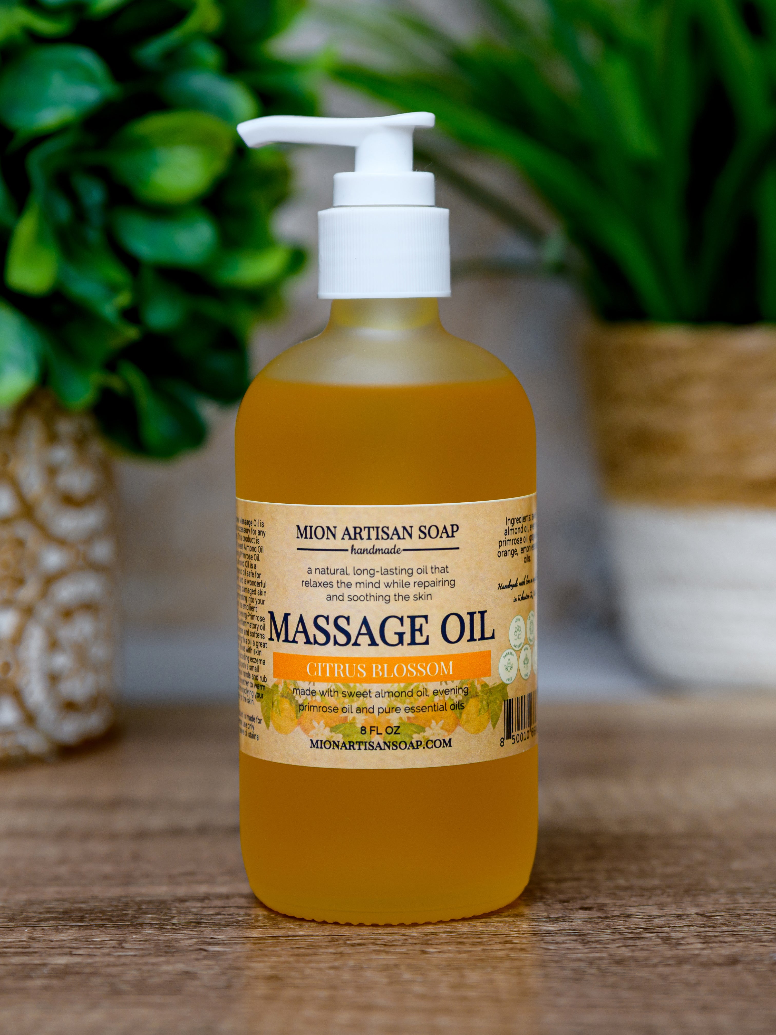 Bottle of Mion Artisan Soap massage oil on a wooden surface with plants in the background