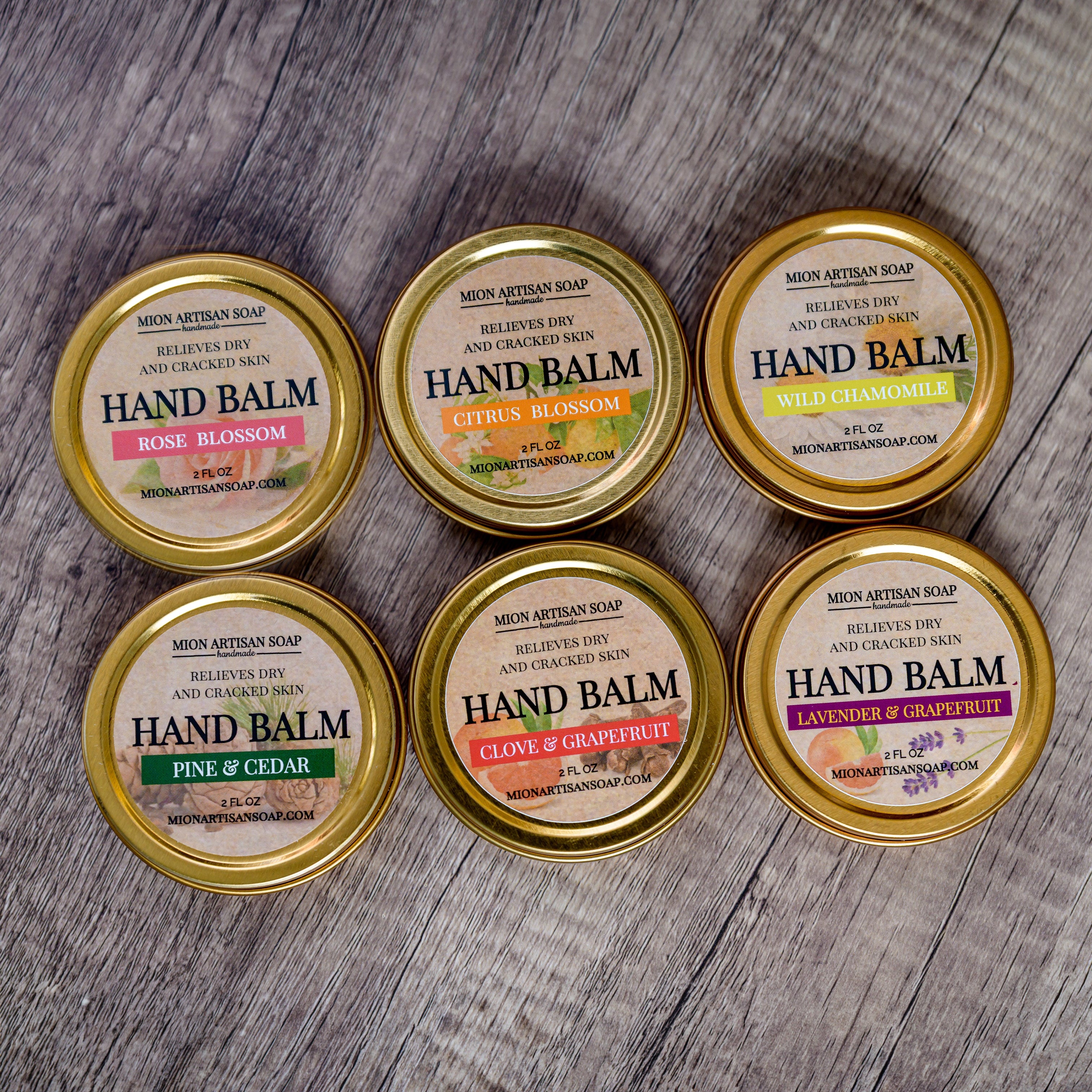 Six tins of hand balm with gold lids on a wooden surface