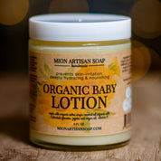 Jar of Mion Artisan Soap organic baby lotion on a wooden surface with a blurred background
